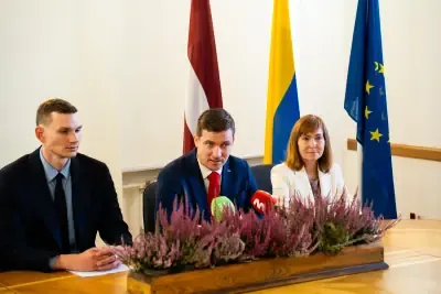 CVK un CERT.LV pārstāvji Mediju brokastīs pie galda ar mikrofoniem; fonā Latvijas un Eiropas Savienības karogi
